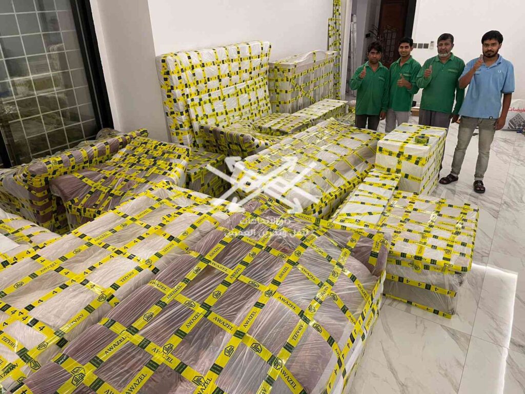 Professional movers wrapping a beige sofa with protective plastic film to prevent dust